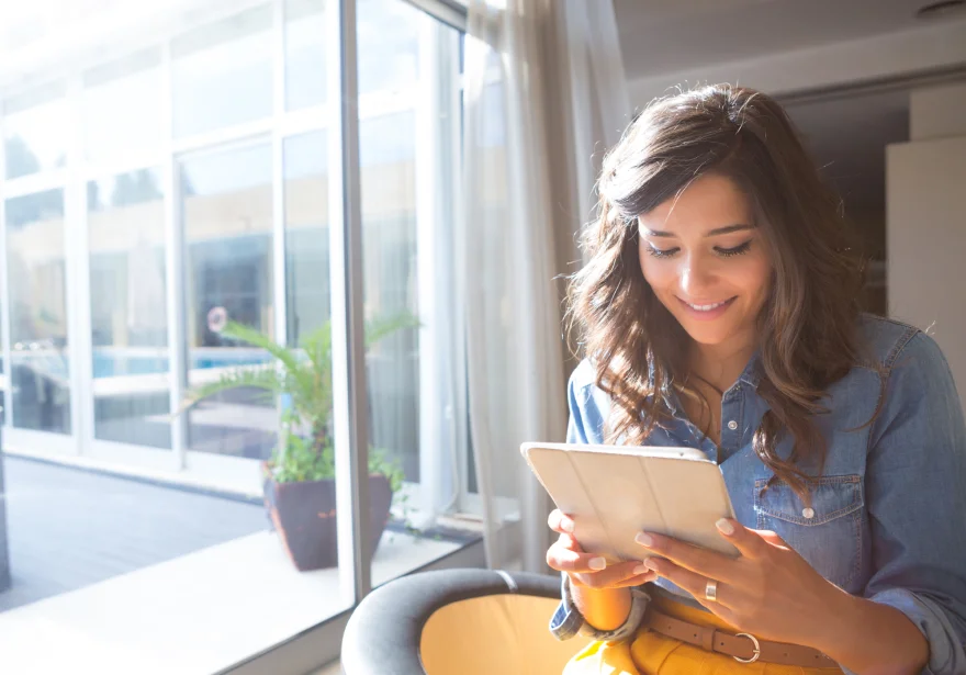 Eine Frau sitzt am Fenster und liest das E-Paper auf ihrem Tablet