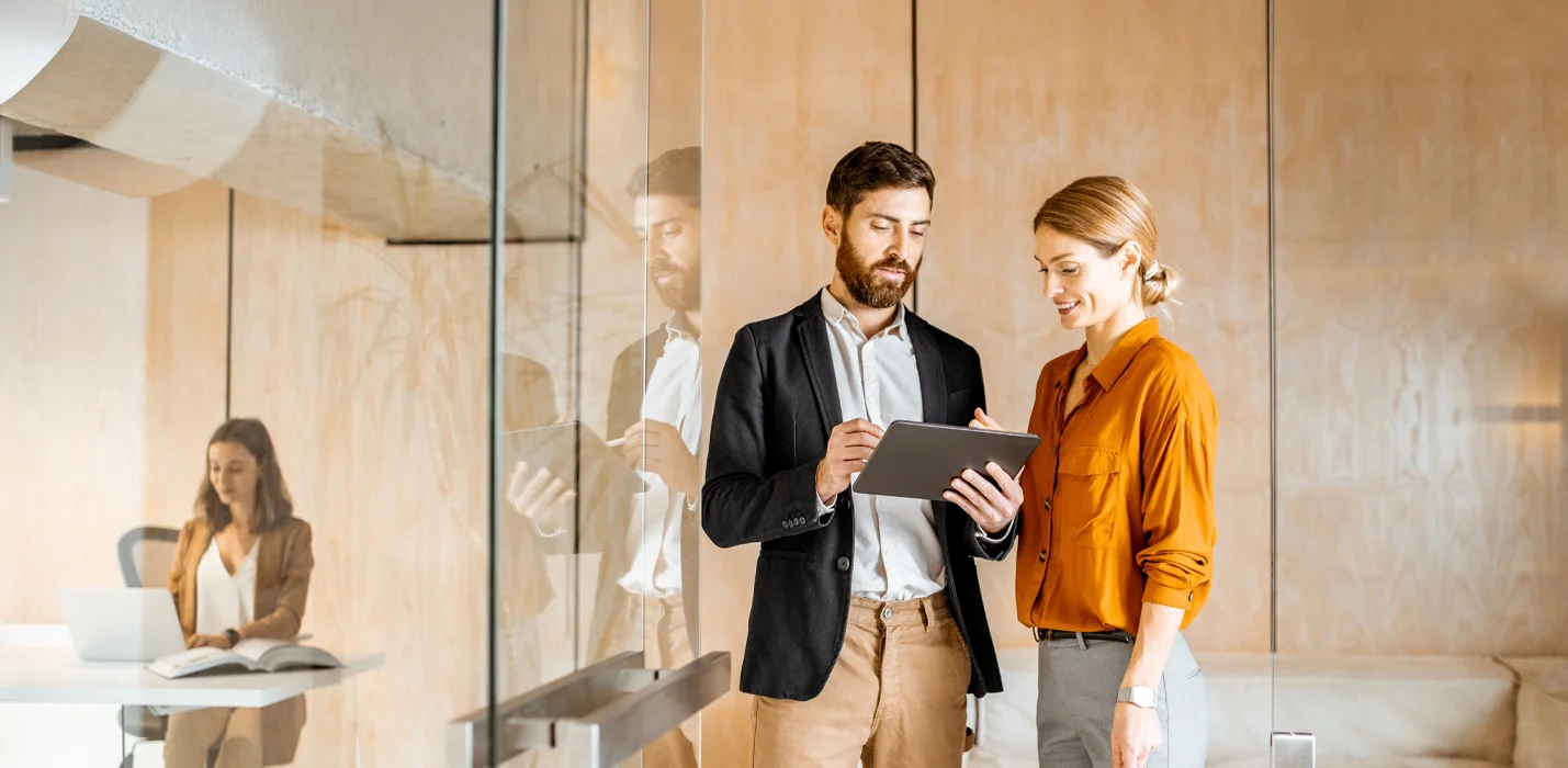 Ein Mann und eine Frau stehen in einem Büro und sehen sich etwas auf einem Tablet an
