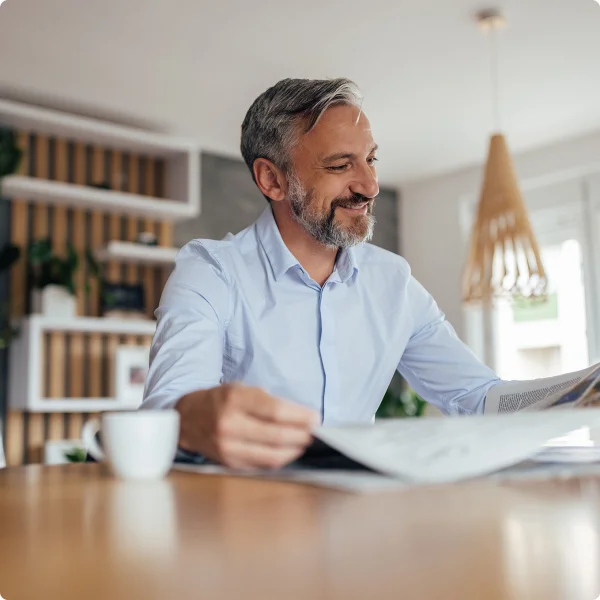 Ein Mann sitzt an einem Tisch und liest Zeitung, daneben steht eine weiße Tasse