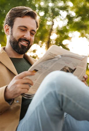 Ein Mann sitzt draußen auf einer Bank und liest Zeitung