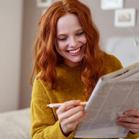 Eine Frau hat eine Zeitung in der Hand auf die sie etwas schreibt